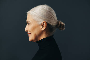 Mature business woman with grey hair looks directly at the camera with a confident and poised expression as she stands in a studio, projecting an air of authority and expertise. - JLPSF30551