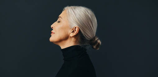 Side view of an empowered senior woman standing tall and confident in a studio setting, dressed in an elegant business attire and silver hair. - JLPSF30552