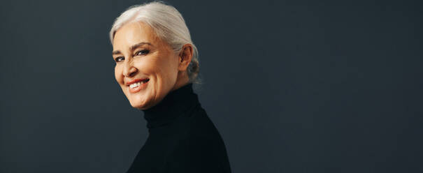 Professional senior woman expressed competence and confidence in a studio portrait, her eyes meeting the camera directly as she smiles warmly and elegantly in her business attire. - JLPSF30553