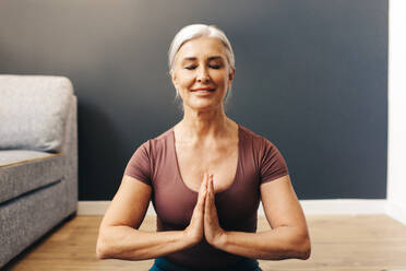 Mature woman practicing yoga meditation at home, she sits in in