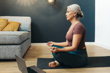 Aging woman meditates in lotus pose, achieving inner peace and embracing the transformative power of yoga in her life. Senior woman practicing a healthy workout routine in her golden years. - JLPSF30577