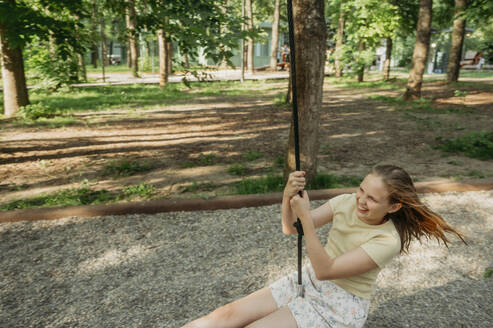 Cheerful girl swinging on swing at park - ANAF01662