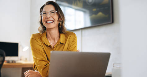 Confident and successful businesswoman, laughs while wearing eyeglasses. Woman celebrating her accomplishments as an entrepreneur and web designer, creating a thriving work environment for herself. - JLPPF02062