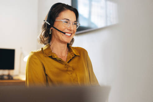 Friendly call center agent answering incoming calls with a headset, providing customer service remotely. Happy woman using her excellent communication skills to resolves customer issues. - JLPPF02071