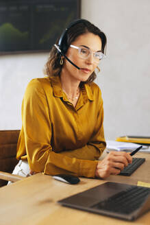 Female call centre agent equipped with a headset offers expert technical support. With her problem-solving abilities, she assists customers with technical issues while sitting in her office. - JLPPF02072