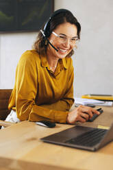 Happy call center agent delivering exceptional customer support from her office desk. Woman attentively listening and resolving customer inquiries through her headset, providing a positive customer experience. - JLPPF02073