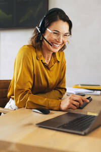 Happy call center agent delivering exceptional customer support from her office desk. Woman attentively listening and resolving customer inquiries through her headset, providing a positive customer experience. - JLPPF02073