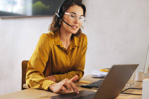 Professional call operator, equipped with a headset, provides remote virtual assistance and customer support. Working from her office desk, she handles customer inquiries and offers efficient solutions. - JLPPF02074