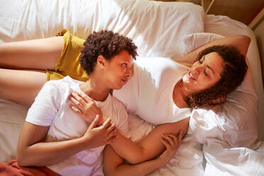 Affectionate lesbian couple cuddling, talking on morning bed - CAIF33395