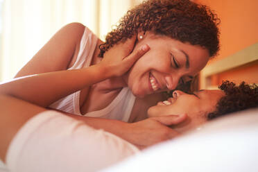 Close up happy affectionate lesbian couple smiling face to face on bed - CAIF33398