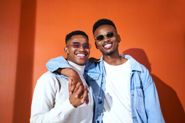 Portrait happy, stylish young gay male couple on orange background - CAIF33403
