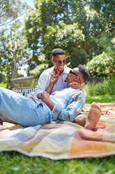Happy young gay male couple cuddling on picnic blanket in park - CAIF33413