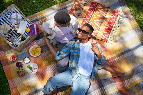 Young gay male couple cuddling, enjoying picnic on blanket in park - CAIF33415