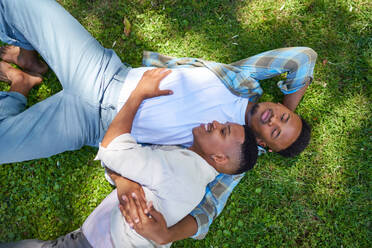 View from above happy, affectionate gay male couple laying in grass - CAIF33420