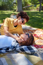 Happy lesbian couple cuddling and talking on picnic blanket in park - CAIF33424