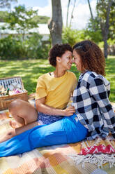 Happy, affectionate lesbian couple on picnic blanket in park - CAIF33428