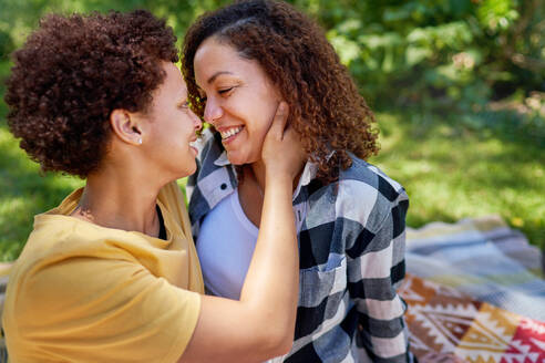 Happy, affectionate lesbian couple hugging face to face in park - CAIF33430