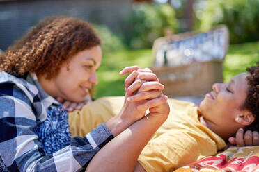 Happy lesbian couple holding hands, enjoying picnic in summer park - CAIF33436