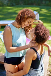 Affectionate lesbian couple with curly hair at summer poolside - CAIF33459