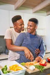 Happy, affectionate young gay male couple cooking and hugging at home - CAIF33461