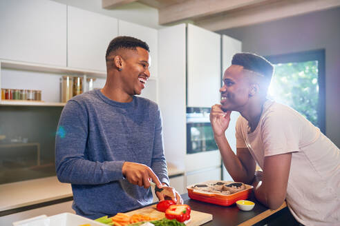 Happy young gay male couple cooking vegetables in kitchen at home - CAIF33463