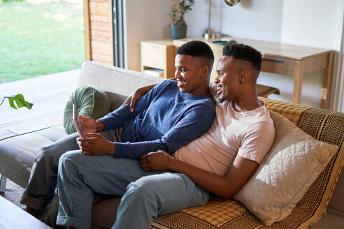 Happy young gay male couple using digital tablet on living room sofa - CAIF33468