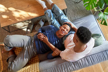 View from above happy young gay male couple cuddling on sofa - CAIF33470