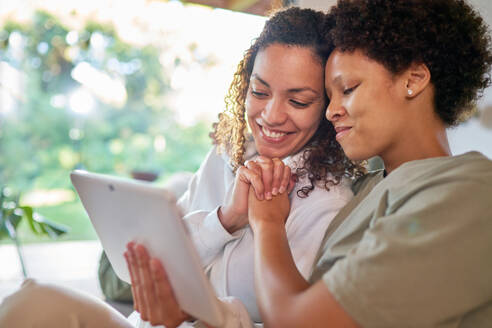 Happy, affectionate lesbian couple holding hands, using digital tablet - CAIF33476