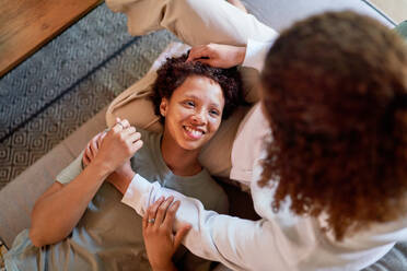 View from above lesbian woman laying in lap of wife on sofa at home - CAIF33478