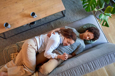 View from above affectionate lesbian couple relaxing, napping on sofa - CAIF33479