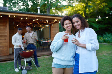 Portrait happy lesbian couple drinking, enjoying barbecue in backyard - CAIF33487