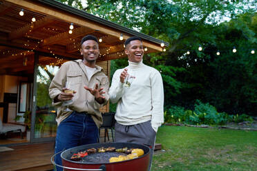 Portrait happy young gay male couple drinking and barbecuing - CAIF33493