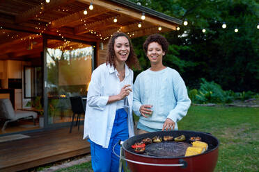 Portrait happy lesbian couple drinking and barbecuing in backyard - CAIF33497