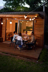 Gay couples enjoying dinner at table on patio with string lights - CAIF33501