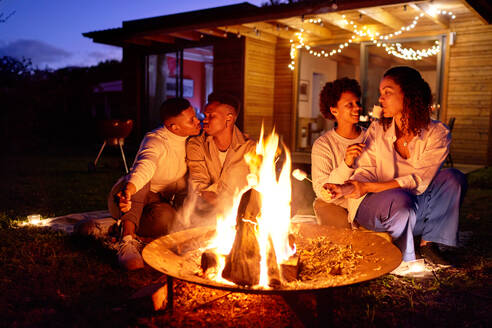 Happy gay couples roasting marshmallows at fire pit in summer backyard - CAIF33505