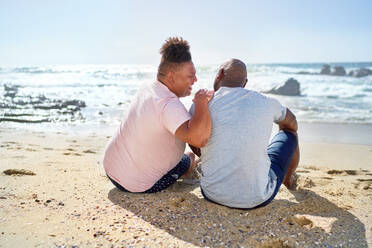 Gay male couple laughing on sunny ocean beach - CAIF33506