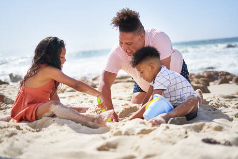 Family making sandcastle on sunny summer ocean beach - CAIF33513