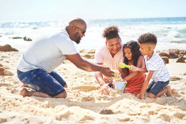 Gay male couple with kids playing in sand on sunny ocean beach - CAIF33518