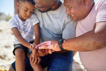 Gay male couple comforting cute son on beach - CAIF33526