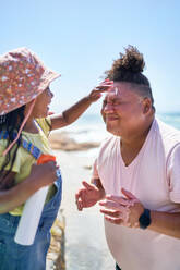 Cute daughter applying sunscreen to face of father on sunny beach - CAIF33527