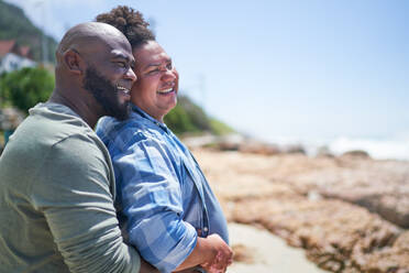 Happy, affectionate gay male couple hugging on sunny summer beach - CAIF33541