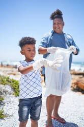 Father and son with rubber gloves cleaning beach together - CAIF33553