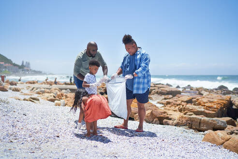 Gay male couple and kids cleaning litter from sunny ocean beach - CAIF33556