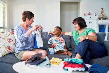 Lesbian couple and son folding laundry and talking in living room - CAIF33557