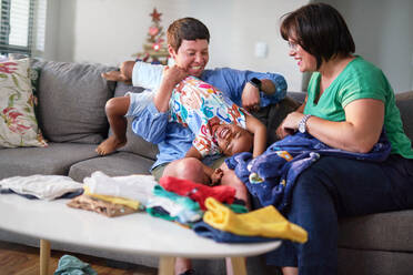 Happy lesbian couple folding laundry, tickling son on living room sofa - CAIF33564