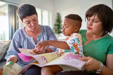 Lesbian couple and son reading story at home - CAIF33570