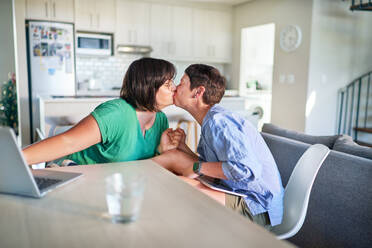 Affectionate lesbian couple kissing face to face at dining table - CAIF33573
