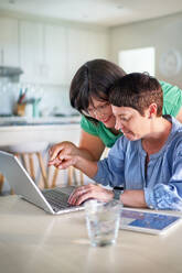 Happy lesbian couple using laptop in dining room at home - CAIF33576