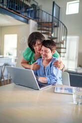 Happy lesbian couple using laptop together at dining table at home - CAIF33577