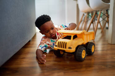 Cute boy playing with dump truck on hardwood floor at home - CAIF33579